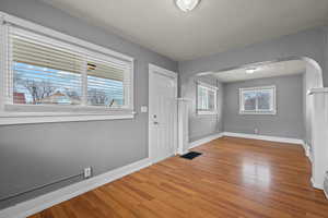 Entryway featuring a textured wall, arched walkways, light wood-style flooring, and a textured ceiling