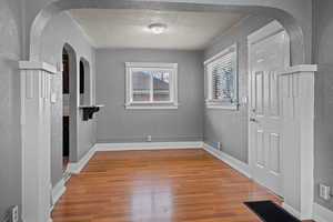 Foyer with a textured wall, arched walkways, light wood-style flooring, and a textured ceiling