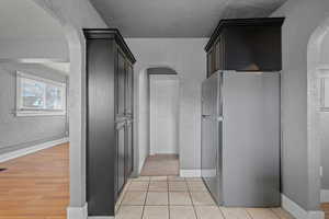 Hall with arched walkways, a textured wall, a textured ceiling, and light tile patterned floors