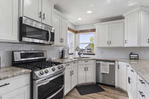 Kitchen with stainless steel appliances, white cabinets, decorative backsplash, light wood finished floors, and light stone counters