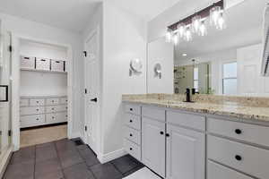 Bathroom featuring a shower stall, vanity, dark tile patterned floors, and a spacious closet