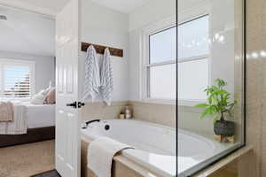 Ensuite bathroom featuring a bath, plenty of natural light, and carpet