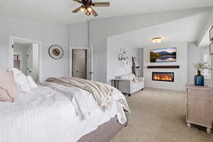 Bedroom featuring a stone fireplace, light colored carpet, lofted ceiling, and a ceiling fan