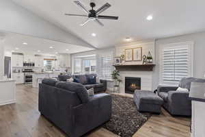 Living area featuring vaulted ceiling, light wood-style flooring, a ceiling fan, a large fireplace, and recessed lighting