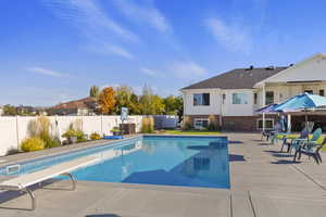 View of pool with patio surround, a diving board, and a fenced backyard