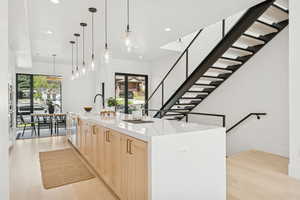 Kitchen with light wood finish cabinets, a spacious island, light wood finished floors, light stone counters, and pendant lighting