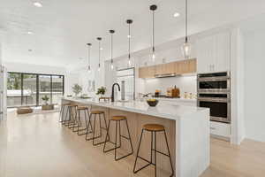 Kitchen featuring a kitchen bar, light wood-type flooring, light wood finish cabinets, stainless steel appliances, and a spacious island