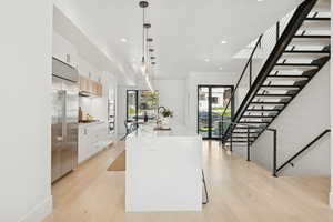Kitchen with a large island, hanging light fixtures, white cabinetry, stainless steel appliances, and light stone counters