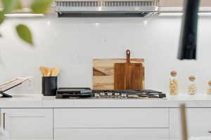 Kitchen view of white cabinets, stainless steel gas cooktop, and light stone countertops