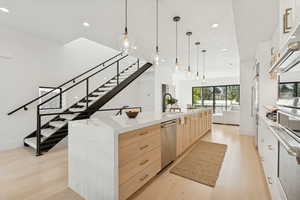 Two tone kitchen with light stone countertops, light wood-style floors, a spacious island, pendant lighting, and stainless steel appliances