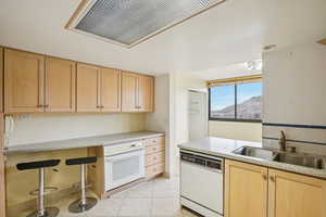 Kitchen with light wood finish cabinets, white appliances, light tile patterned flooring, a breakfast bar area, and a mountain view