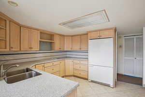 Kitchen with light wood finish cabinets, freestanding refrigerator, light tile patterned flooring, light stone counters, and electric stovetop