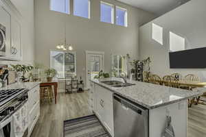 Kitchen with white cabinetry, light stone countertops, stainless steel appliances, light wood-style flooring, and a kitchen island with sink