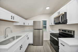 Kitchen featuring stainless steel appliances, white cabinets, light wood-style floors, and light stone countertops