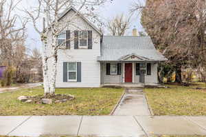 View of front of property with a front lawn, a chimney, roof with shingles, and a porch