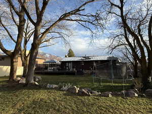 Back of property with a deck with mountain view, a trampoline, and a lawn