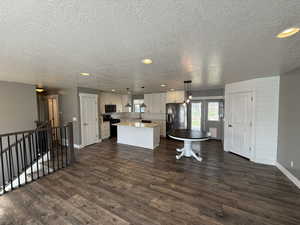 Kitchen featuring decorative light fixtures, black appliances, white cabinetry, a kitchen island, and dark wood-style flooring