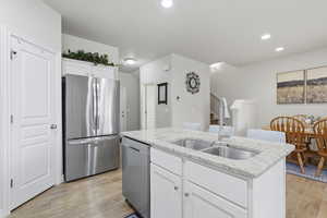 Kitchen featuring white cabinetry, stainless steel appliances, a center island with sink, light stone countertops, and light wood finished floors