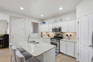 Kitchen featuring stainless steel appliances, white cabinets, light stone counters, a breakfast bar, and light wood-style flooring