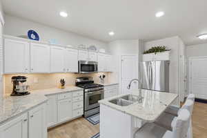 Kitchen with stainless steel appliances, white cabinetry, light wood finished floors, and recessed lighting