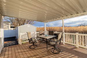 Wooden terrace featuring outdoor dining space, a storage unit, and a fenced backyard