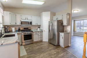 Kitchen with stainless steel appliances, vaulted ceiling, light stone counters, dark wood finished floors, and white cabinetry