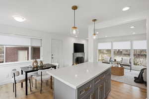 Kitchen with a kitchen island, decorative light fixtures, light wood finished floors, and a fireplace