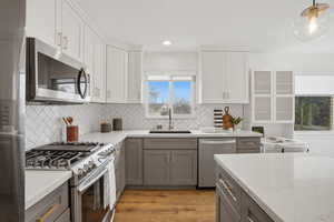 Kitchen featuring stainless steel appliances, two tone cabinets, light stone countertops, light wood finished floors, and pendant lighting