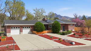 Single story home with driveway, brick siding, an attached garage, a mountain view, and a chimney