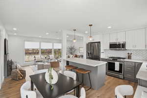 Kitchen featuring stainless steel appliances, dual tone cabinetry, light wood-style floors, open floor plan, and decorative light fixtures