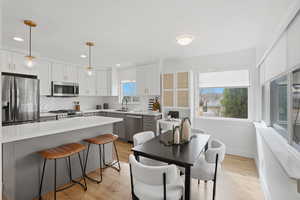 Kitchen featuring stainless steel appliances, light wood-style floors, dual tone cabinetry, decorative backsplash, and a breakfast bar