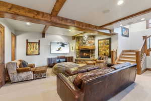Living area featuring light colored carpet, recessed lighting, a stone fireplace, and beamed ceiling