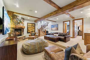 Living area featuring a stone fireplace, beam ceiling, recessed lighting, and light carpet