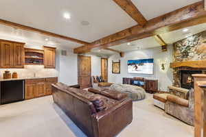 Living area featuring light colored carpet, a fireplace, recessed lighting, bar with sink, and beamed ceiling