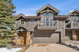 View of front of property featuring stone siding, a balcony, a garage, and concrete driveway
