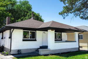 View of front of home with brick siding, roof with shingles, and a chimney