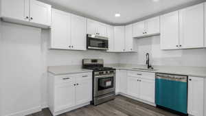 Kitchen featuring white cabinets, stainless steel appliances, dark wood-style floors, and light stone countertops