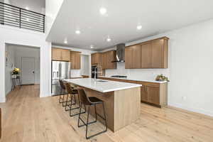 Kitchen with a breakfast bar, stainless steel appliances, an island with sink, light wood LVP finished floors, and recessed lighting
