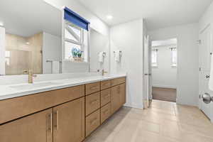 Bathroom featuring double vanity, light tile flooring, and tiled shower