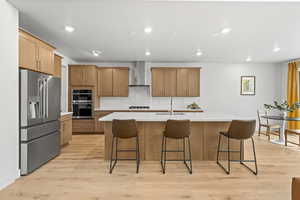 Kitchen featuring stainless steel appliances, light wood LVP flooring, a kitchen bar, recessed lighting, and a center island with sink