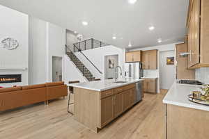 Kitchen featuring a breakfast bar area, light wood LVP flooring, open floor plan, stainless steel appliances, and a glass covered fireplace