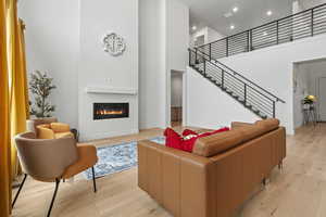 Living room featuring a high ceiling, light LVP wood flooring, a glass covered fireplace, and plenty of natural light