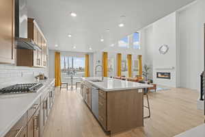 Kitchen with stainless steel appliances, a kitchen island with sink, a kitchen breakfast bar, light wood LVP floors, recessed lighting a high ceiling