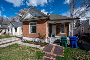 View of front of home with a front lawn, brick siding, a chimney, a shingled roof, and a porch