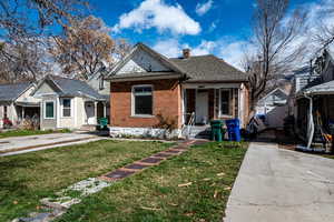 Bungalow-style home with a front lawn, a chimney, brick siding, and a shingled roof