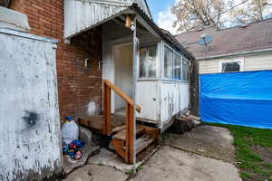Doorway to property featuring brick siding, a sunroom, and a deck