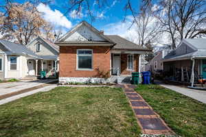 View of front of home featuring a porch, a front yard, brick siding, and a chimney