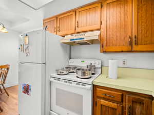 Kitchen with white appliances, light countertops, wood finish cabinets, and light wood-type flooring