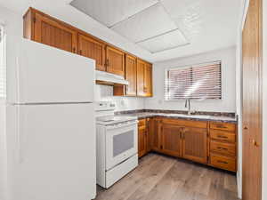 Kitchen with white appliances, dark countertops, light wood-style floors, and wood finish cabinetry