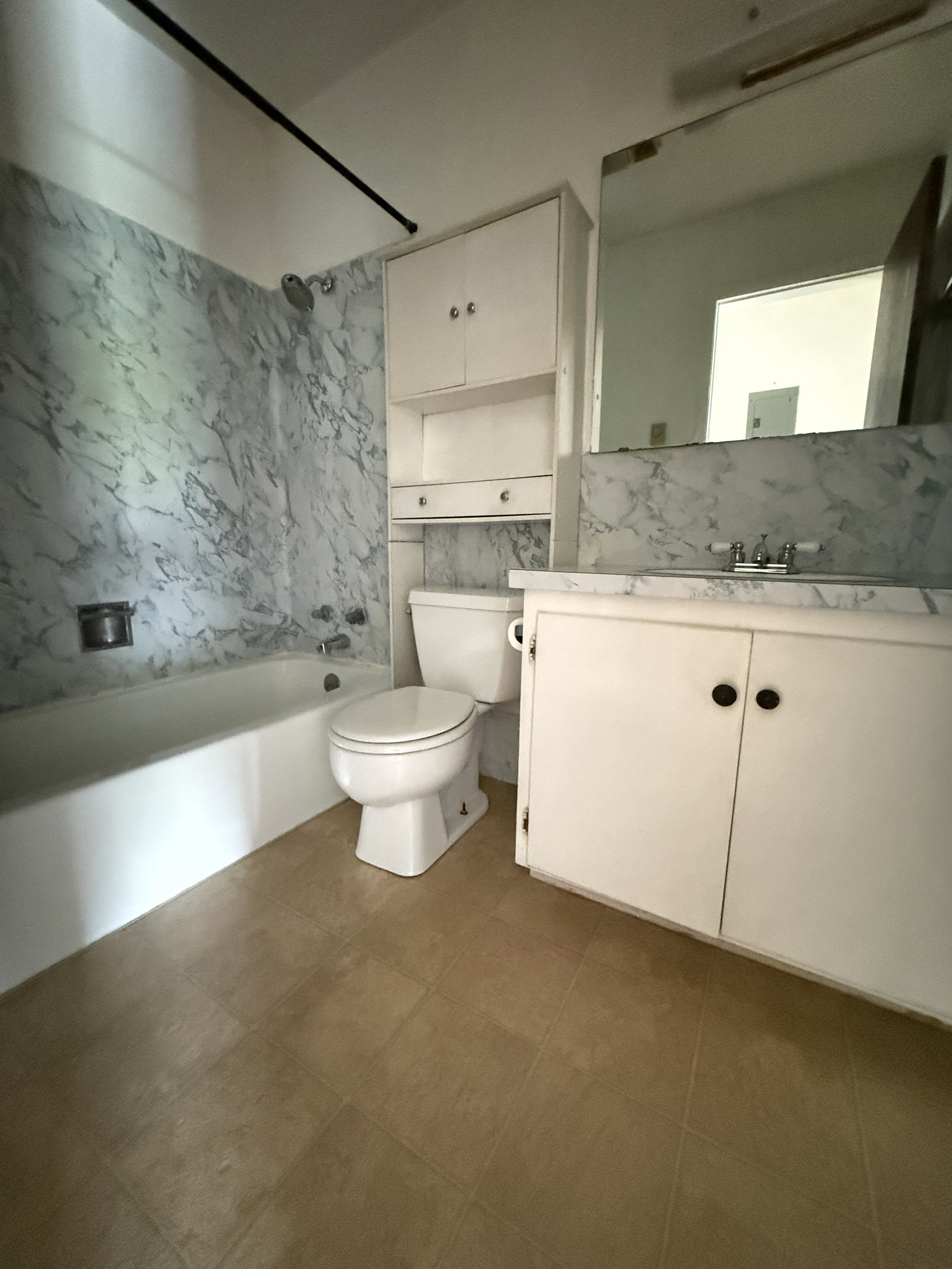 Bathroom featuring a white bathtub with marble-look wall surround, a white toilet, and a white vanity with integrated sink and marble-look countertop